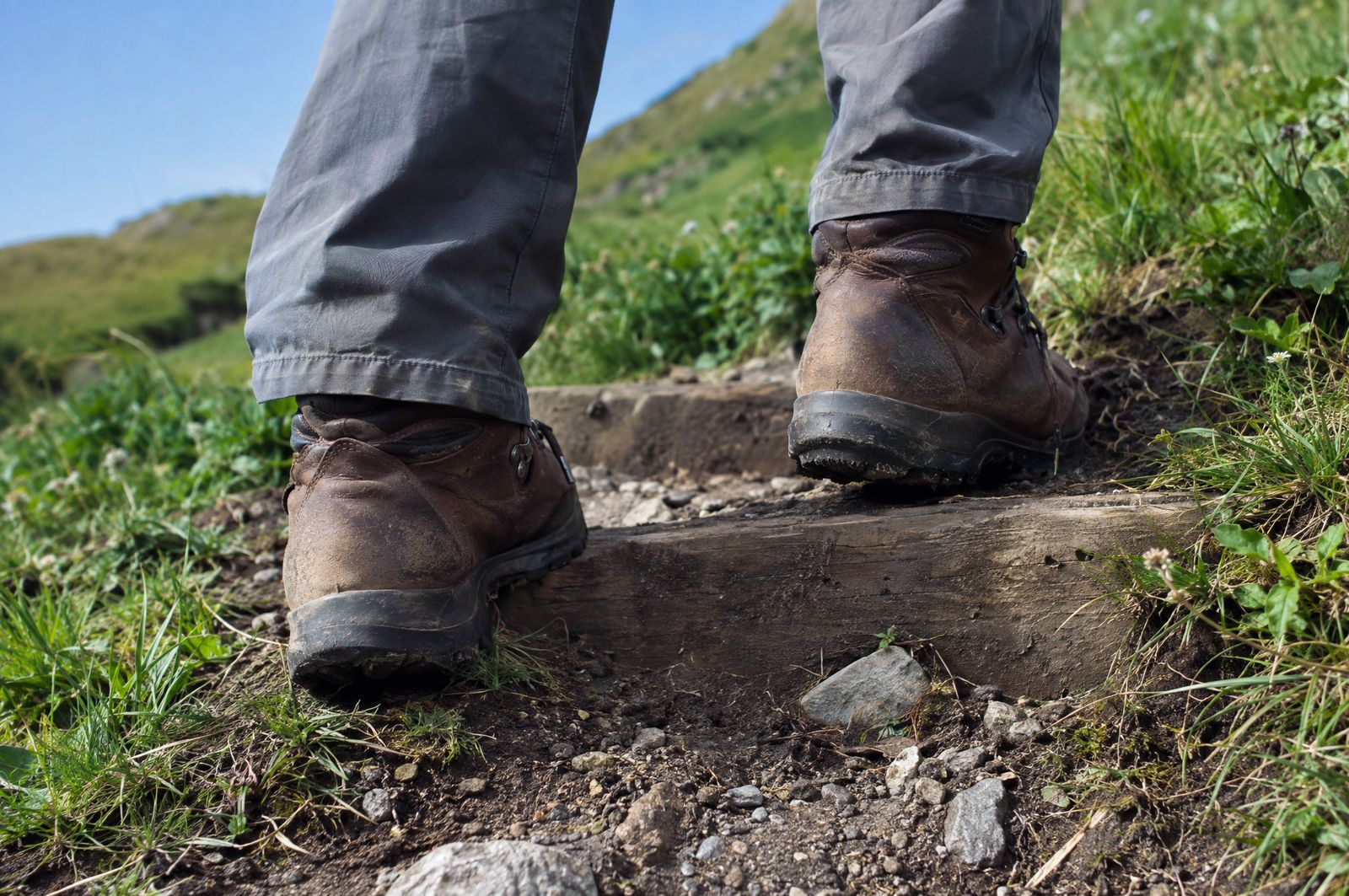 Worn brown leather walking boots stepping up onto a wooden step set into a hillside trail